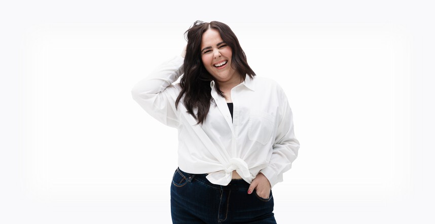 Woman wearing a white button up shirt, and jeans, stands in front of a white background